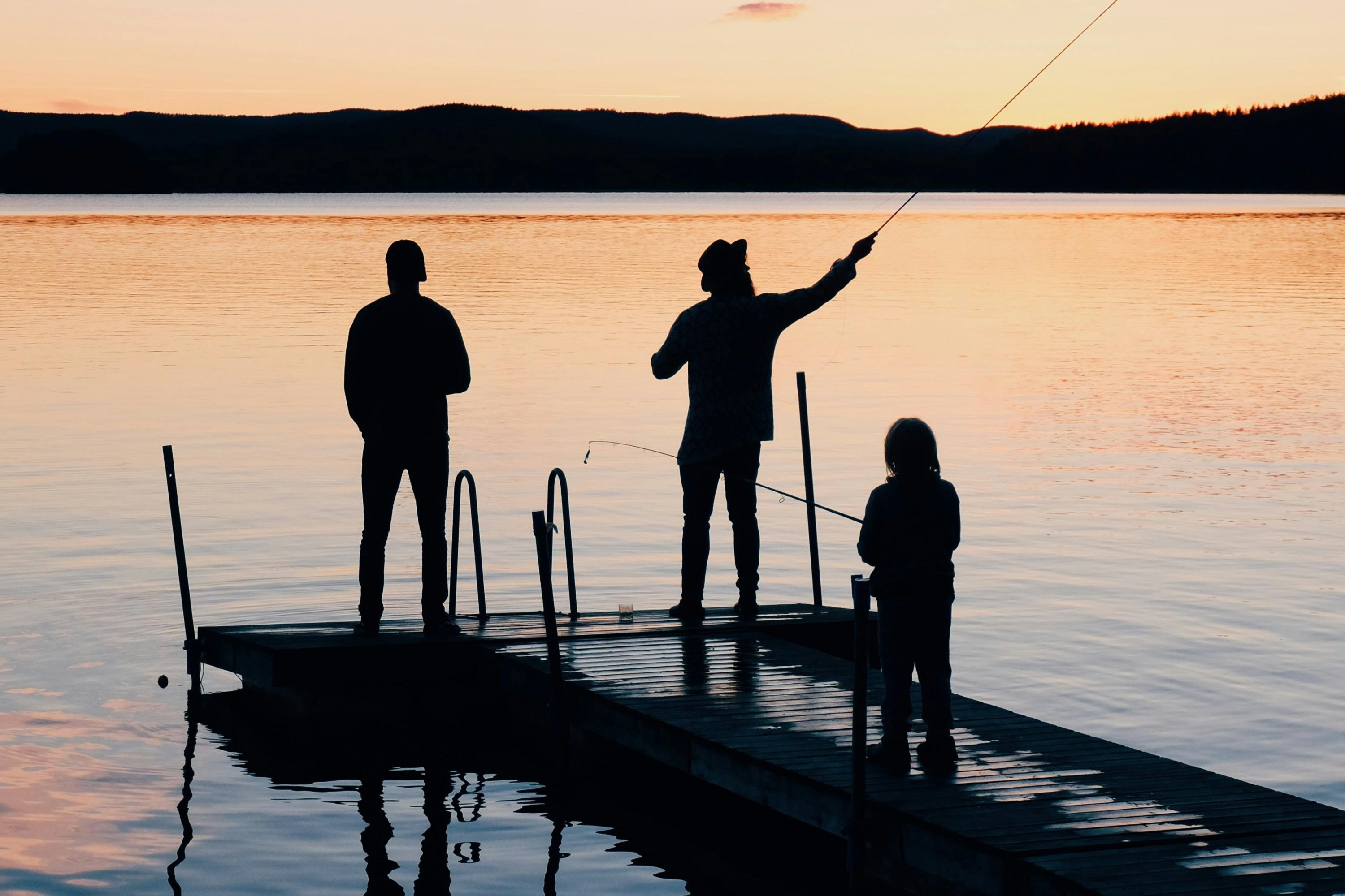 3 persons fishing on a dock facing a sunset