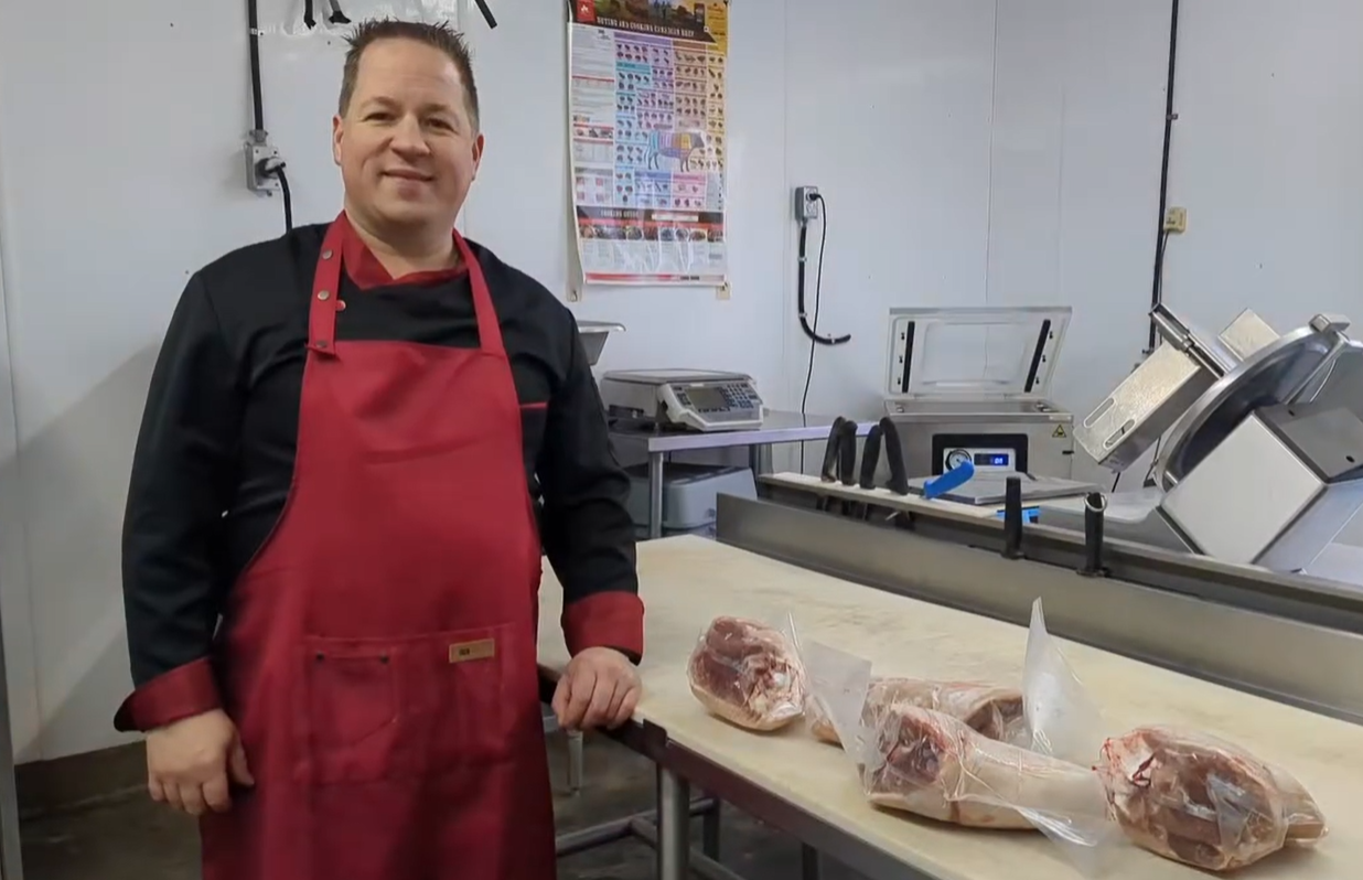Owner Benoit Bonneau standing at a counter in the shop with cuts of meat on the table 