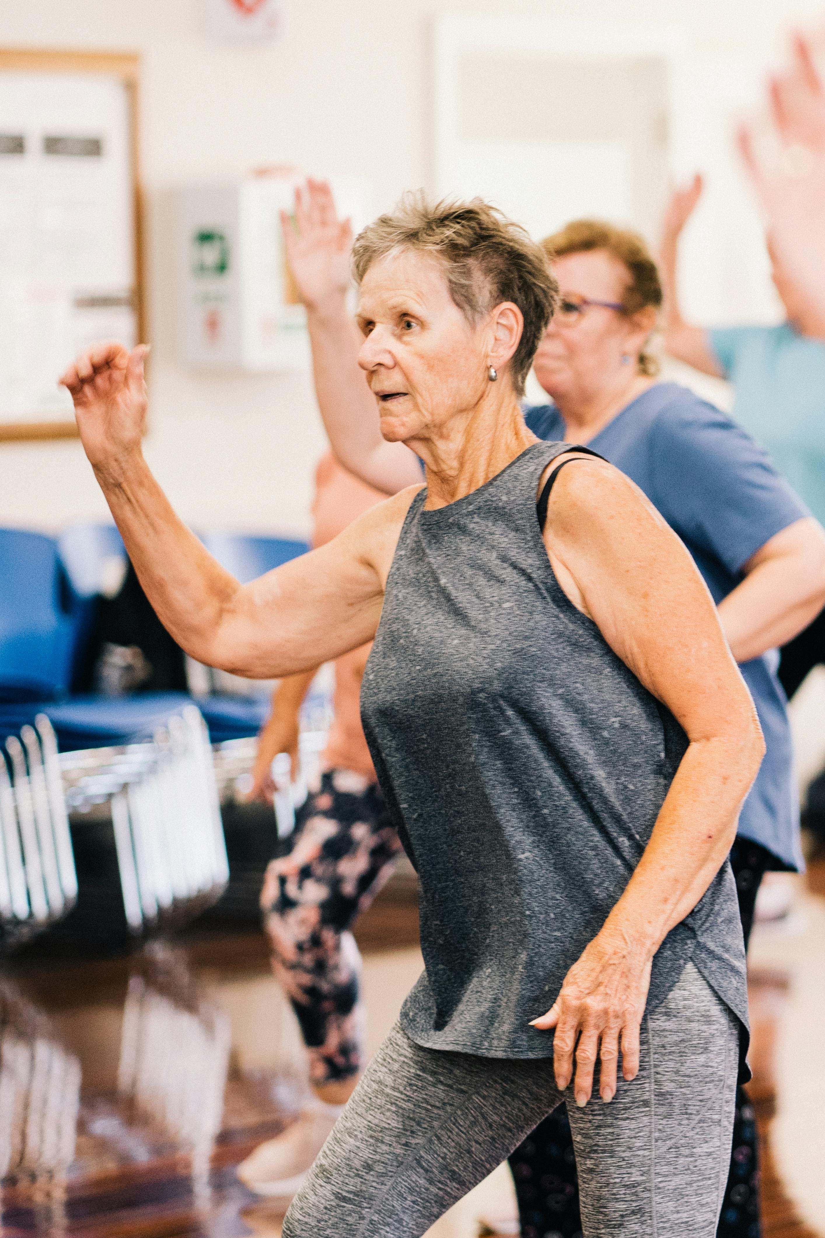 A lady 55 years old and older exercising and following someone's lead.