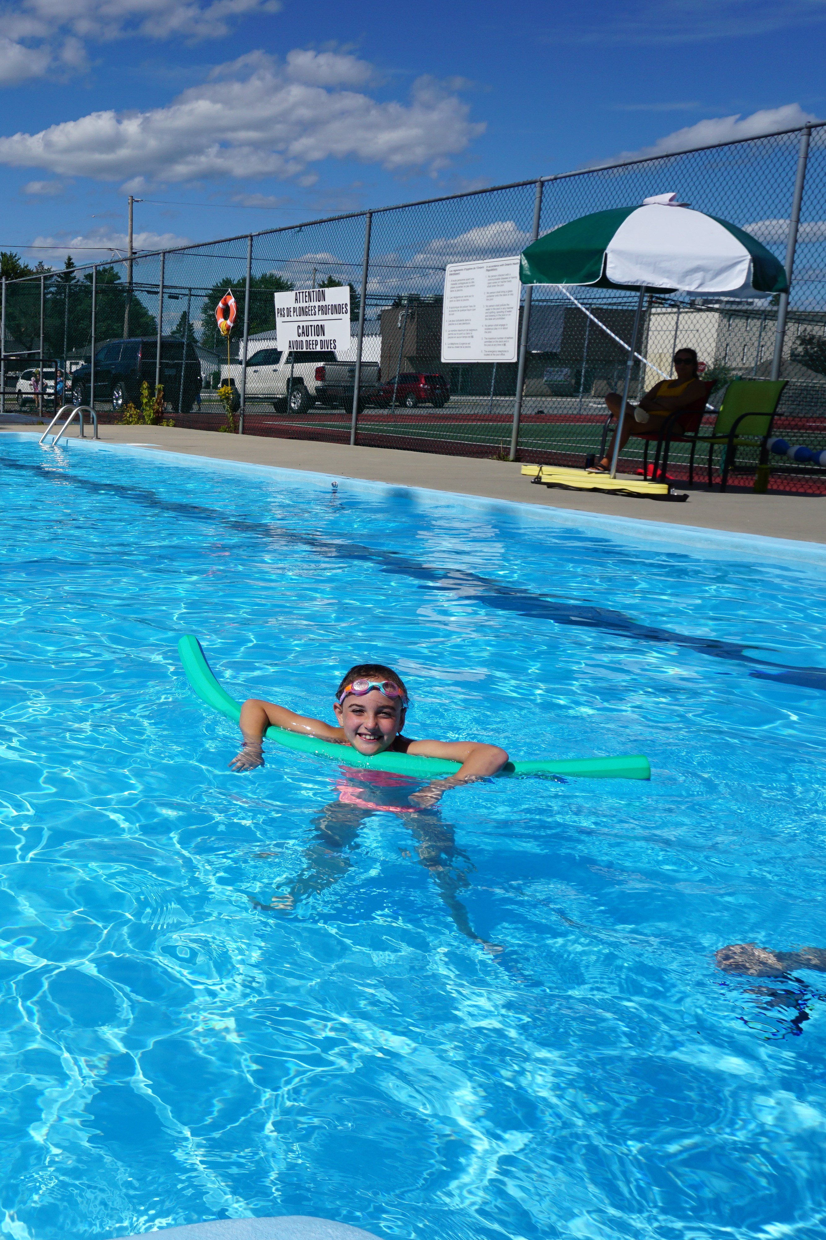 Little girl in a swimming pool with goggles and a noodle. 