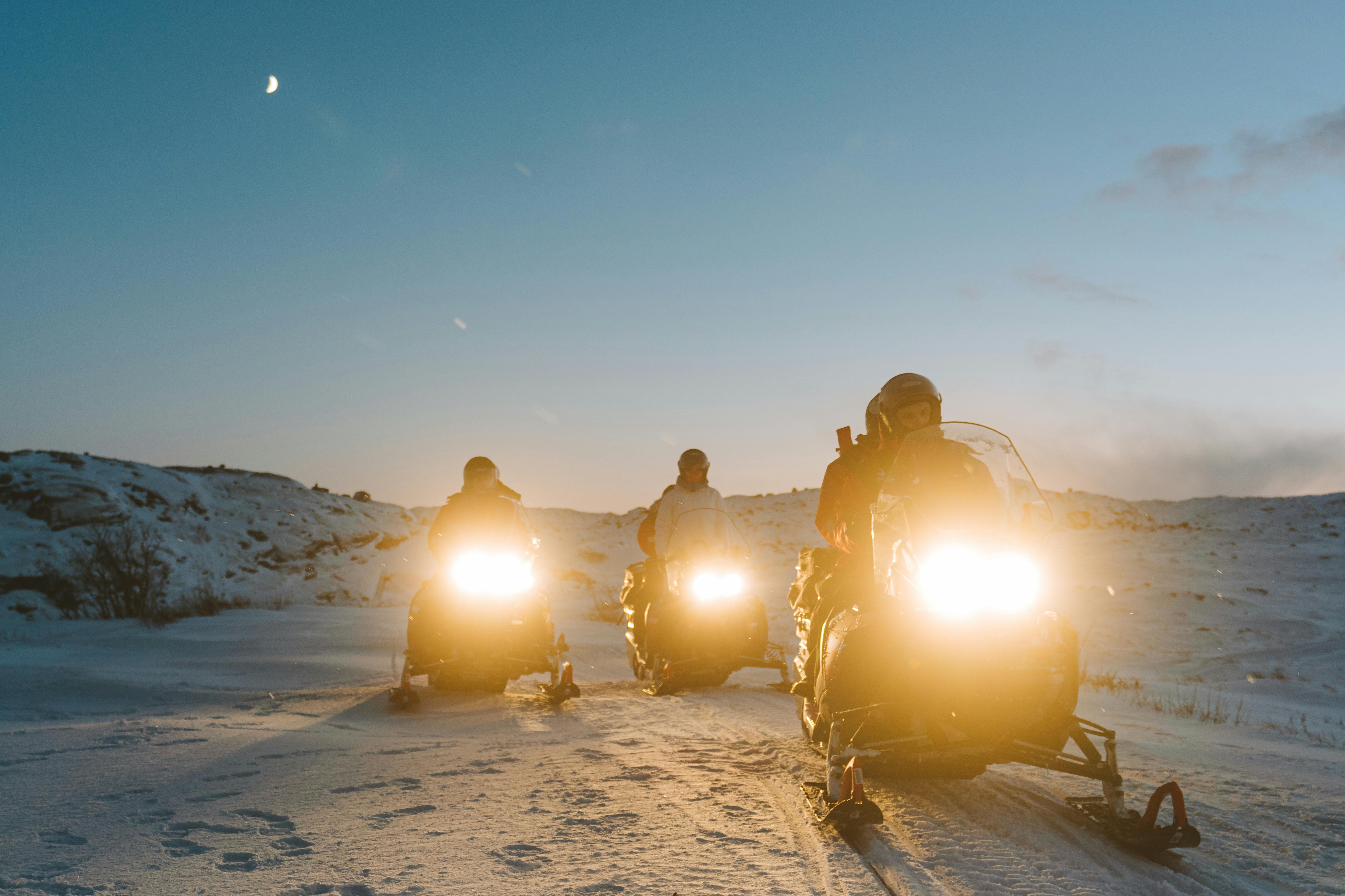 Three people riding snowmobile towards the camera. 