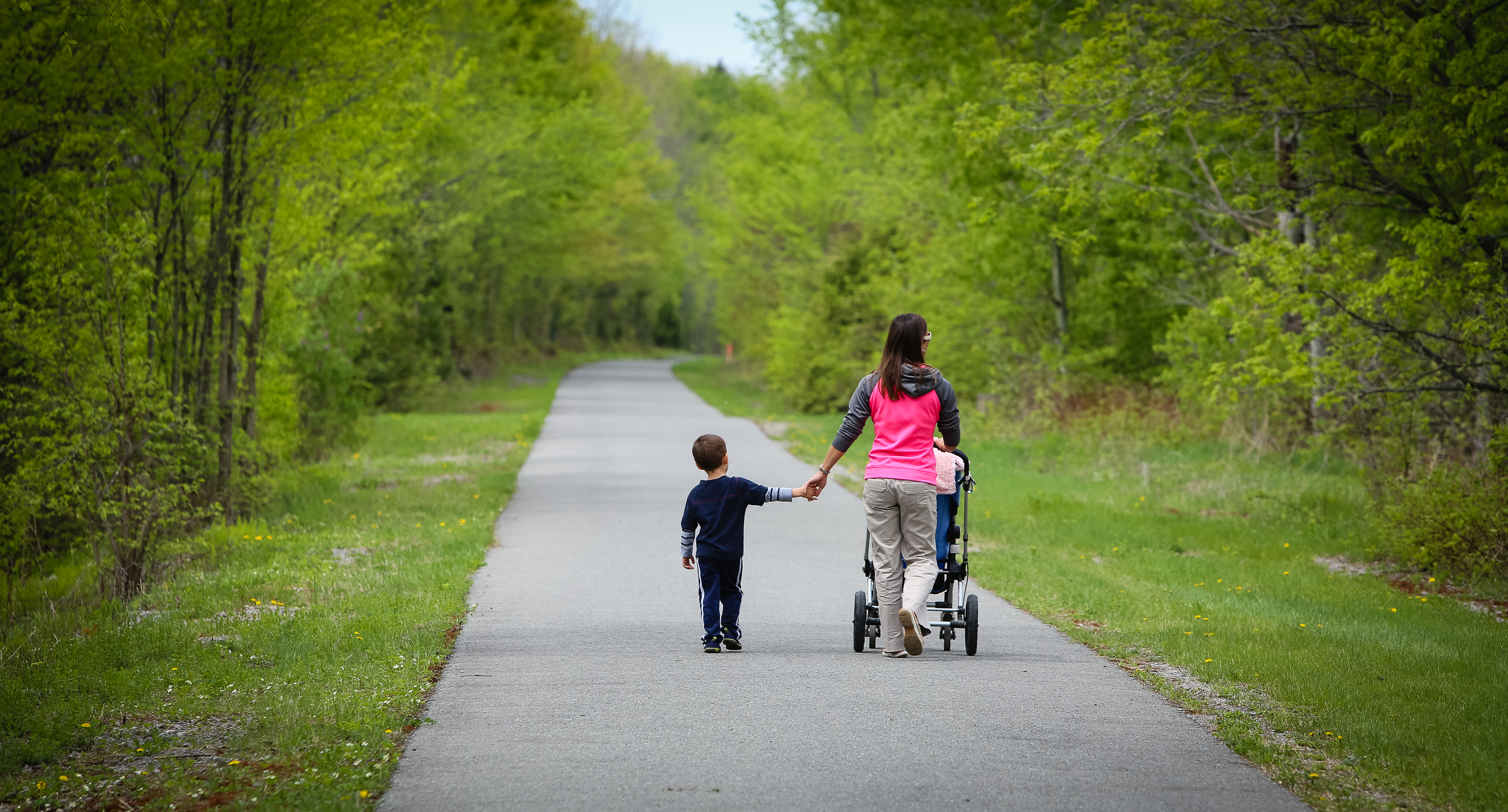 Mother and child walking on footpath bordered by grass and trees