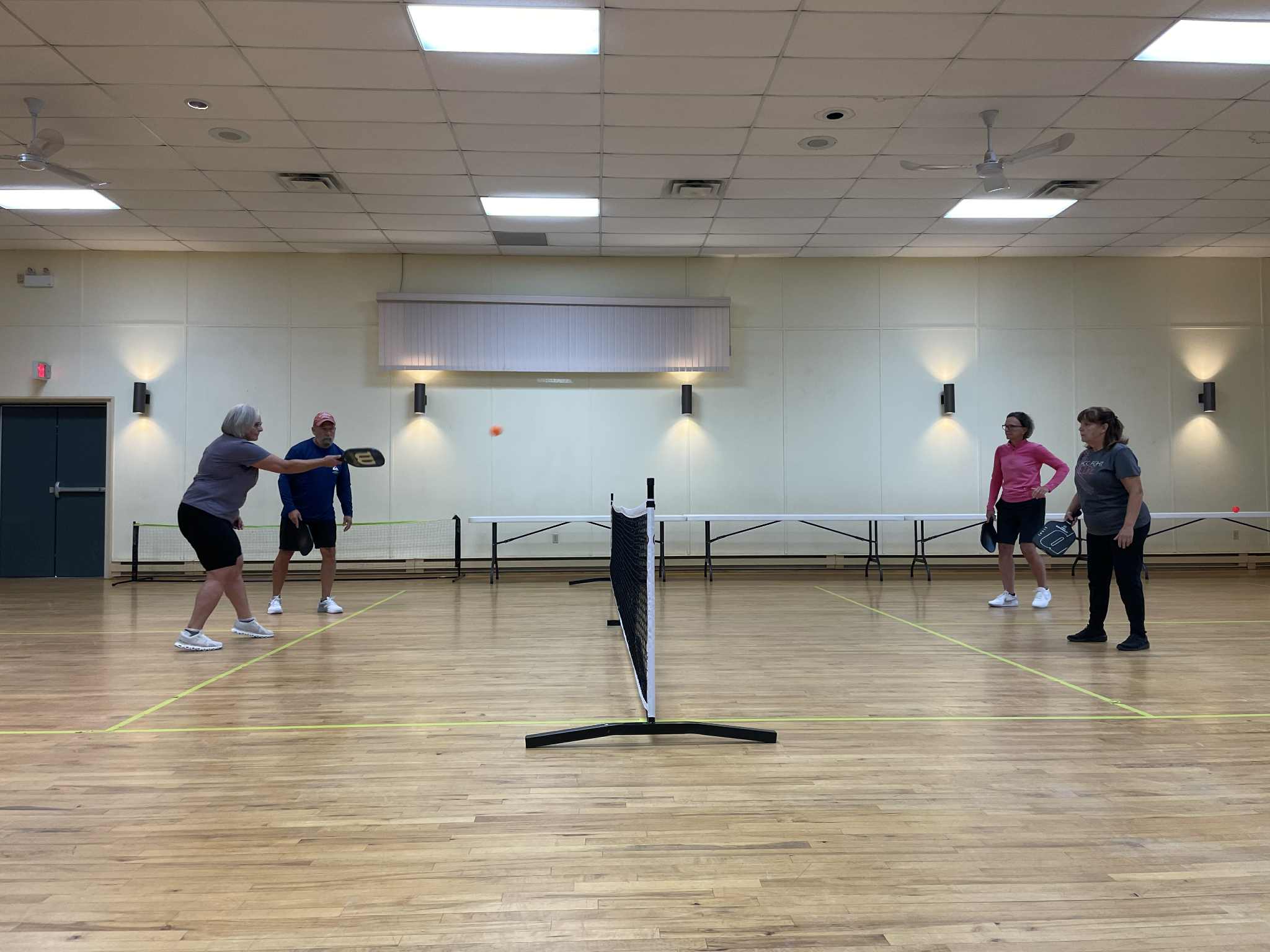 Un groupe de 4 ainés jouent au pickleball dans une salle communautaire 