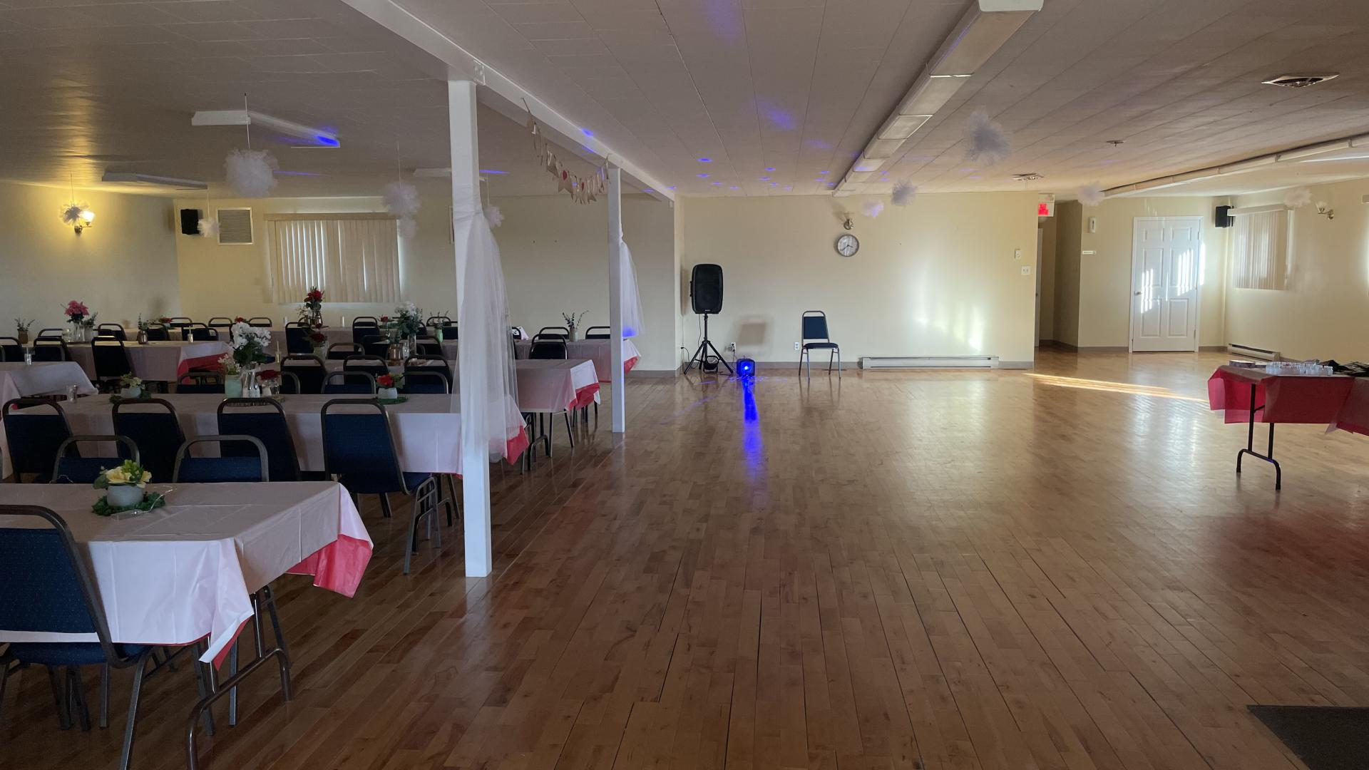 Spacious hall with wooden floor, tables, and chairs arranged along the walls.