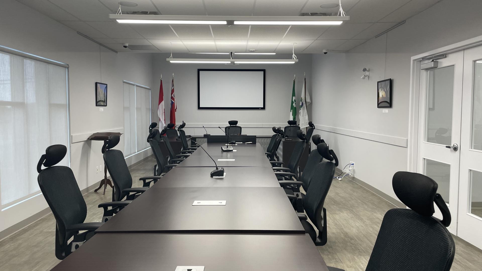 Large conference room with long table and office chairs, screen at the far end.