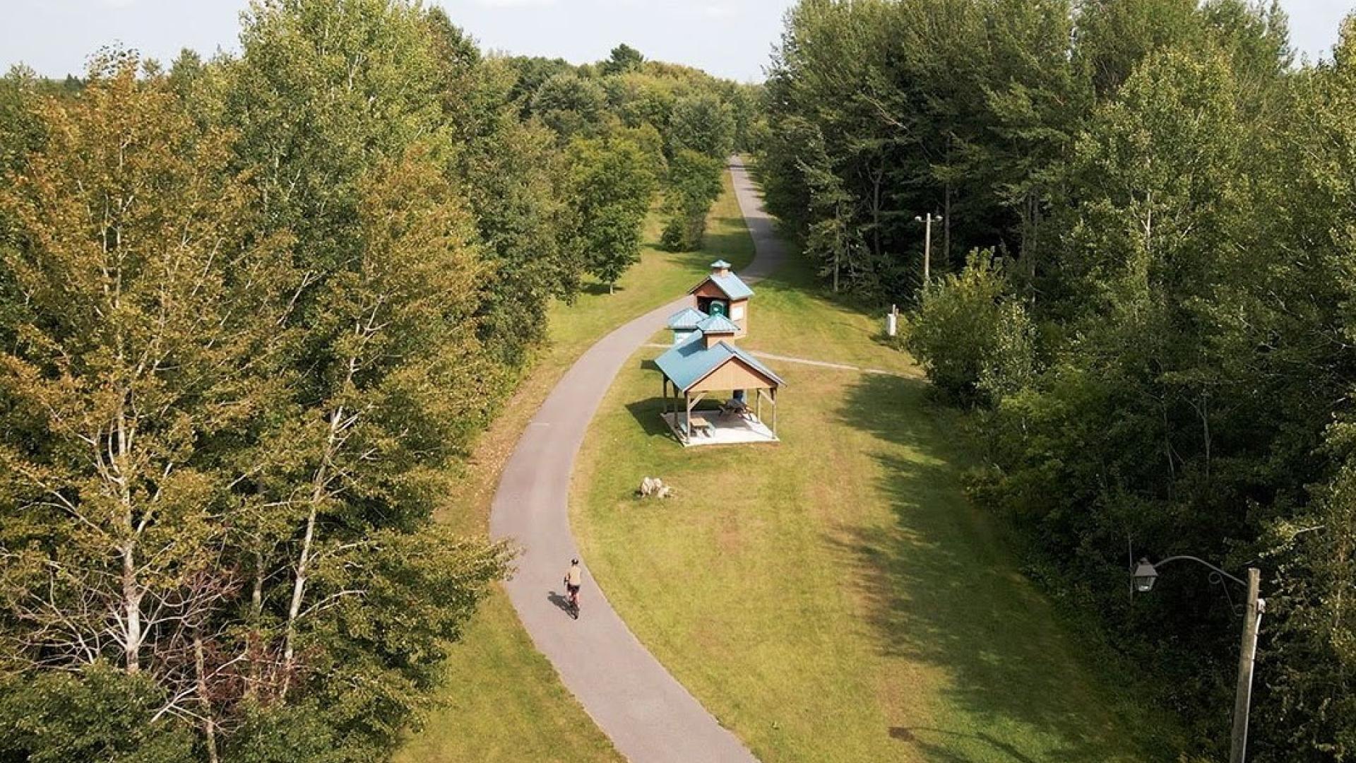 Pathway through a park with trees and two small shelters.