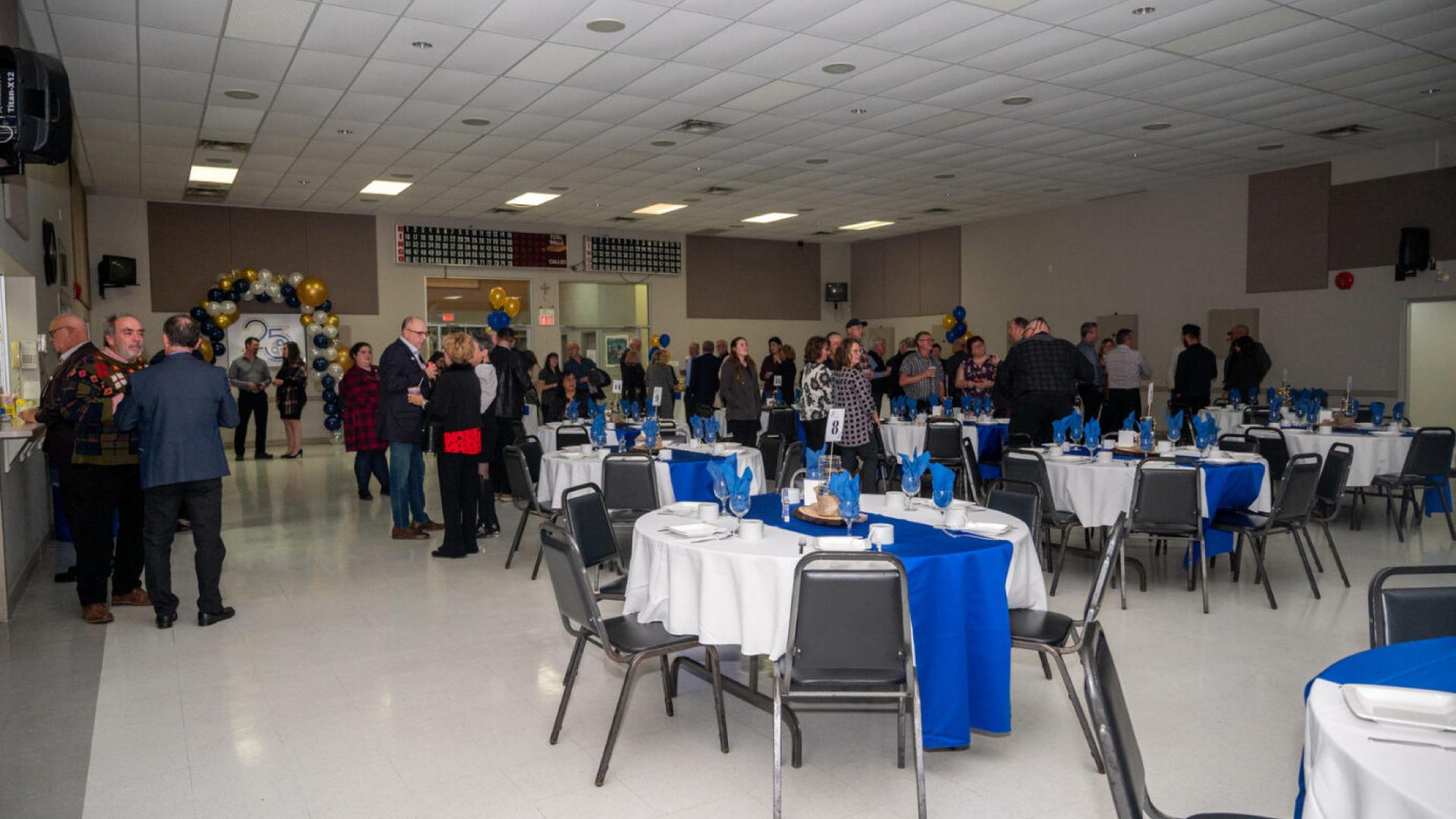 Banquet hall with people mingling and tables set with blue and white linens.
