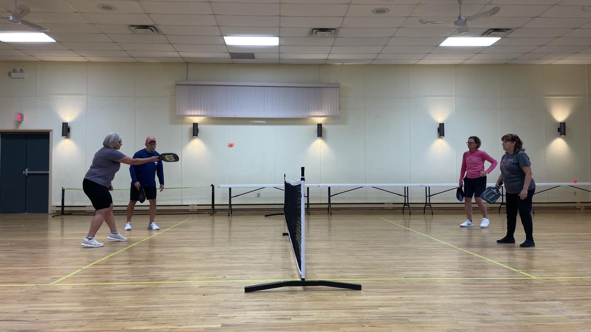 Group of four people in a indoor hall playing pickleball