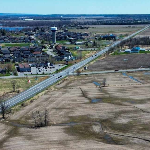 Aerial view of a road dividing a residential area and open fields, with a river on the left.
