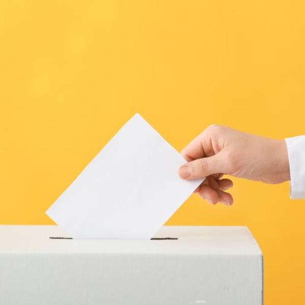 Close-up of a person’s hand dropping a voting ballot into a ballot box.